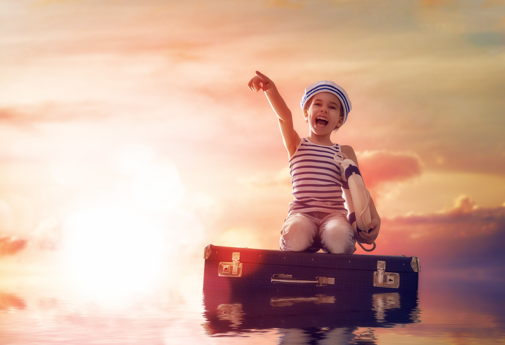Dreams of travel! Child floats on a suitcase against the backdrop of a sunset.